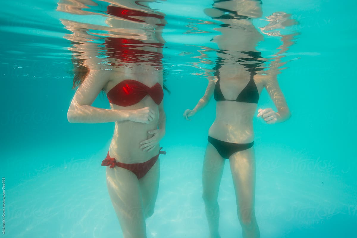 Two woman distorted body underwater in swimming pool.