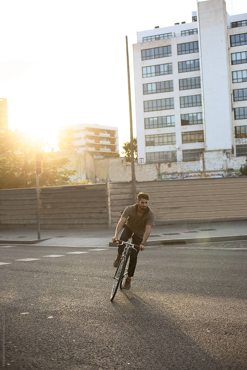 Young man riding a  bicycle in the streets of a city at sunset