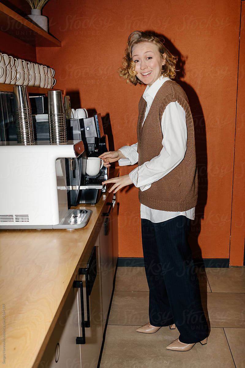 Happy woman brewing coffee in workplace
