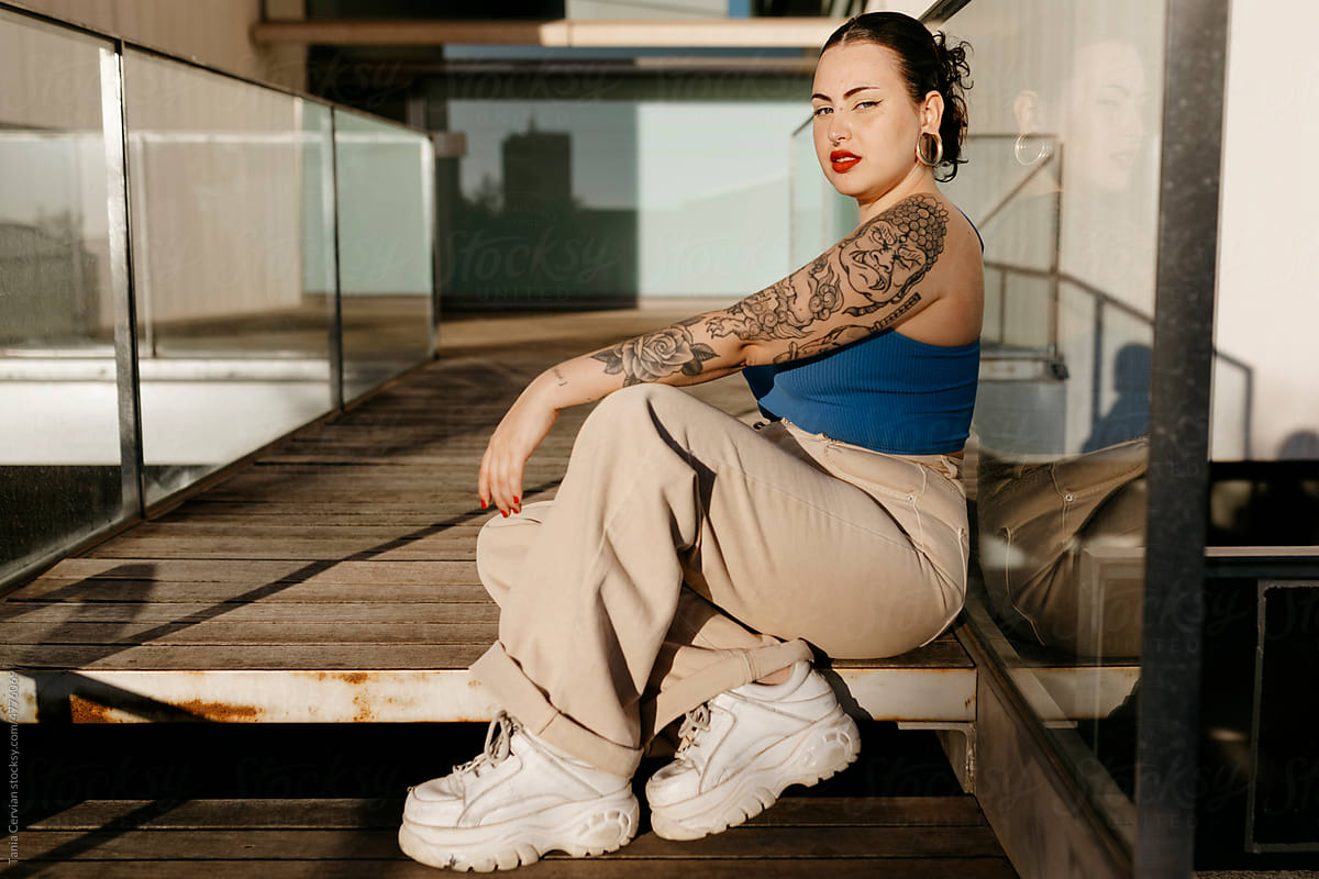 Confident tattooed woman sitting on staircase in city