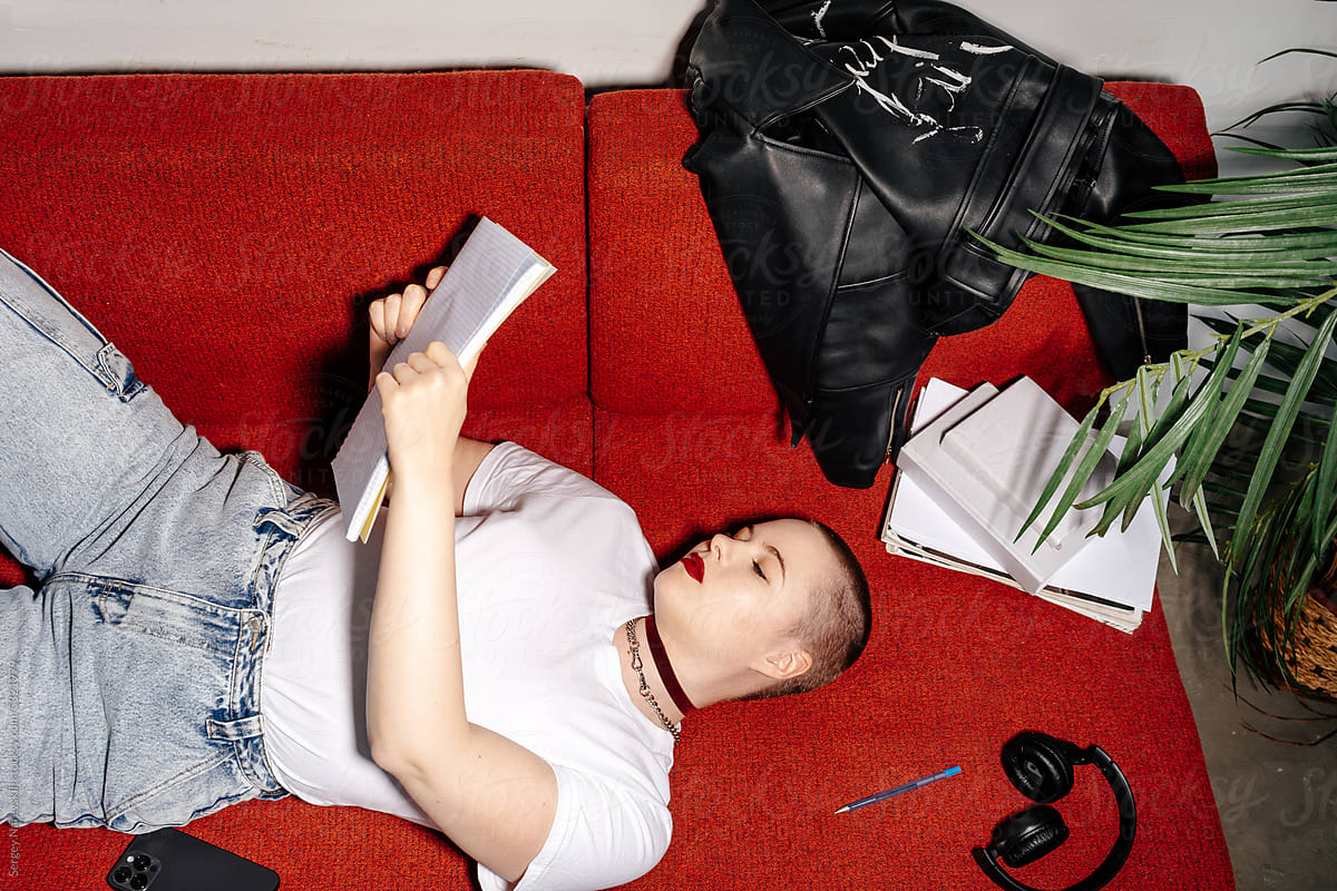Female student lying on sofa and reading notes in notebook