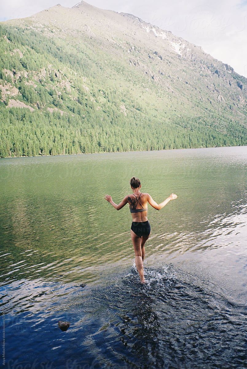 Woman running into the cold mountain lake in summer