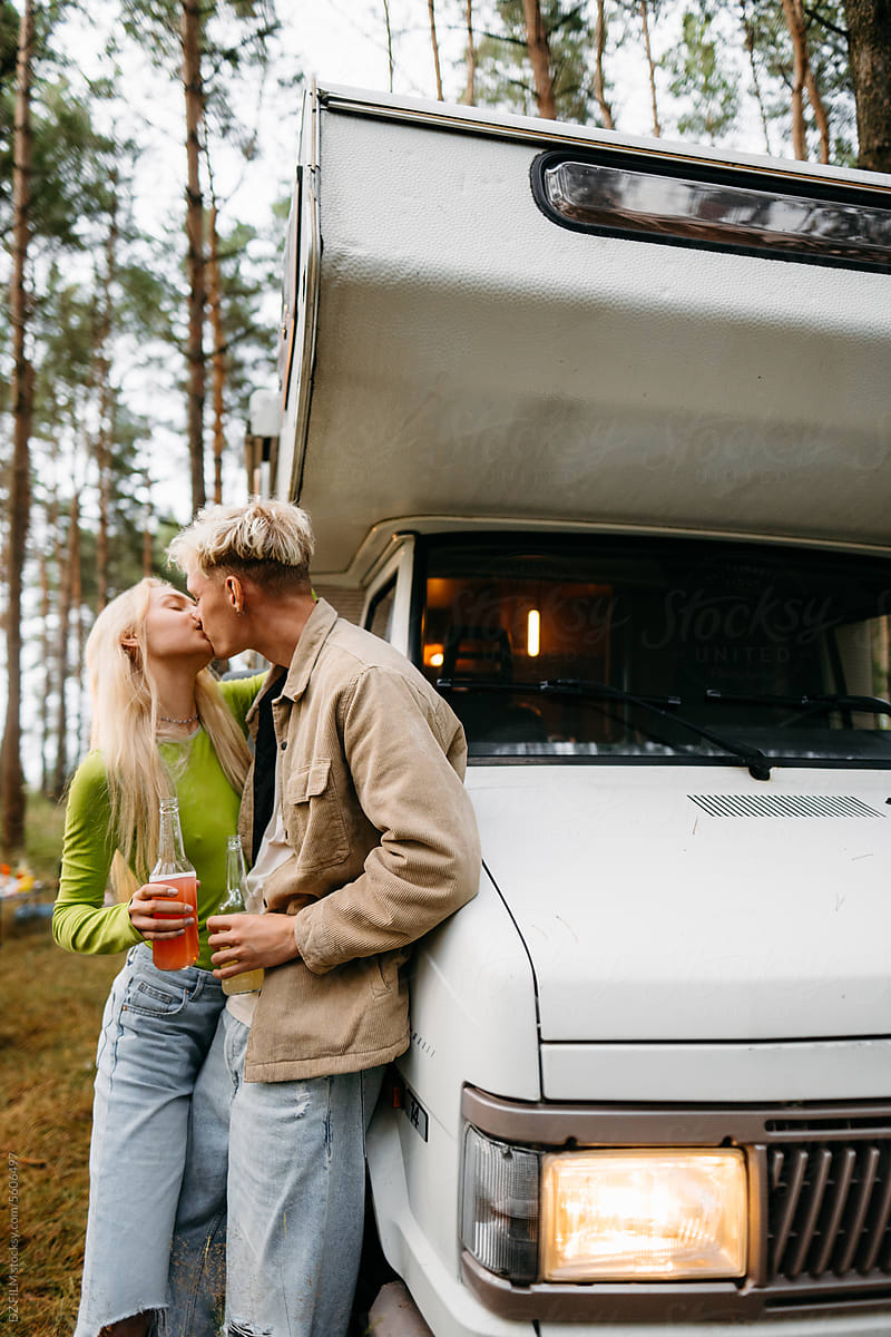 A man and a woman kiss standing near a van