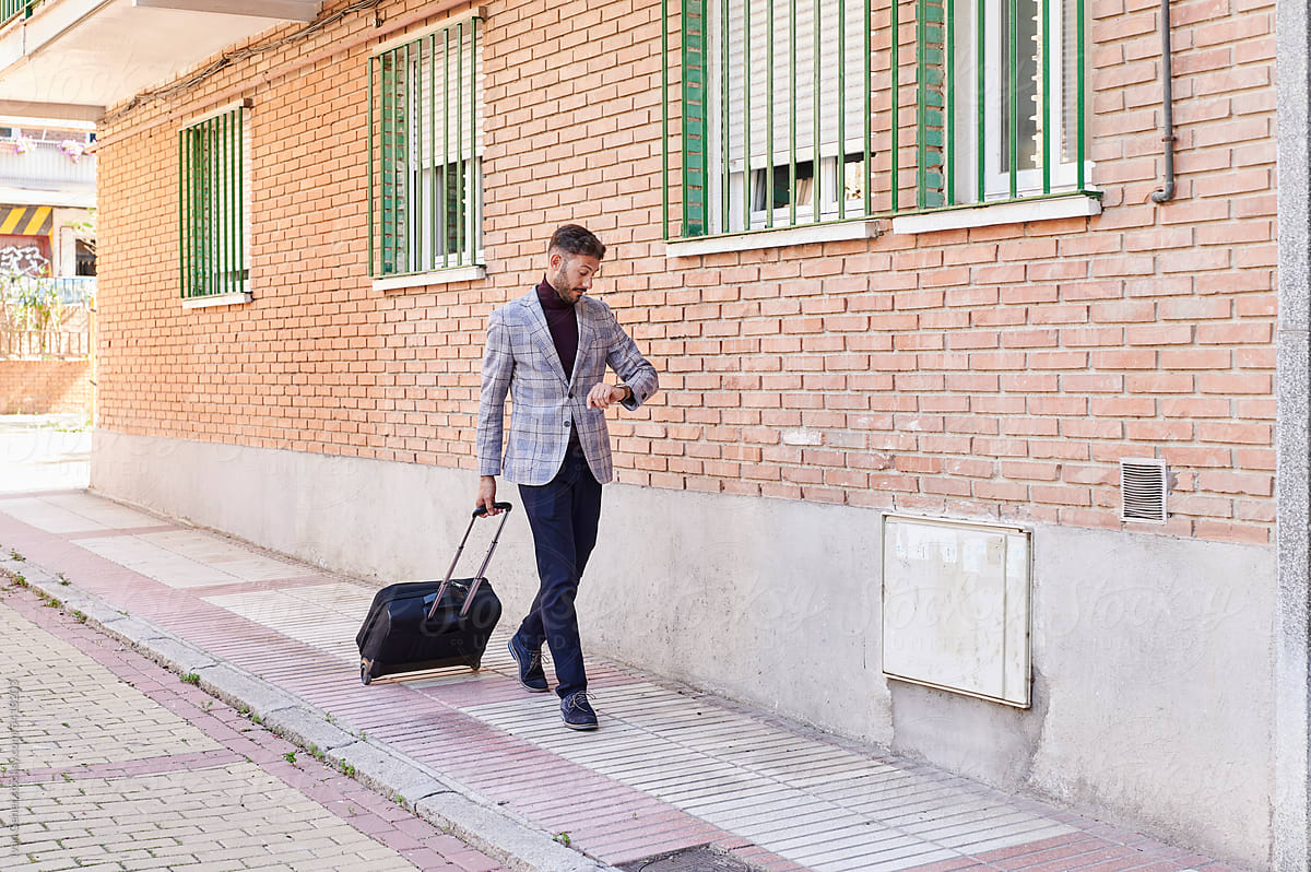 Man with a suitcase checking the time outdoors