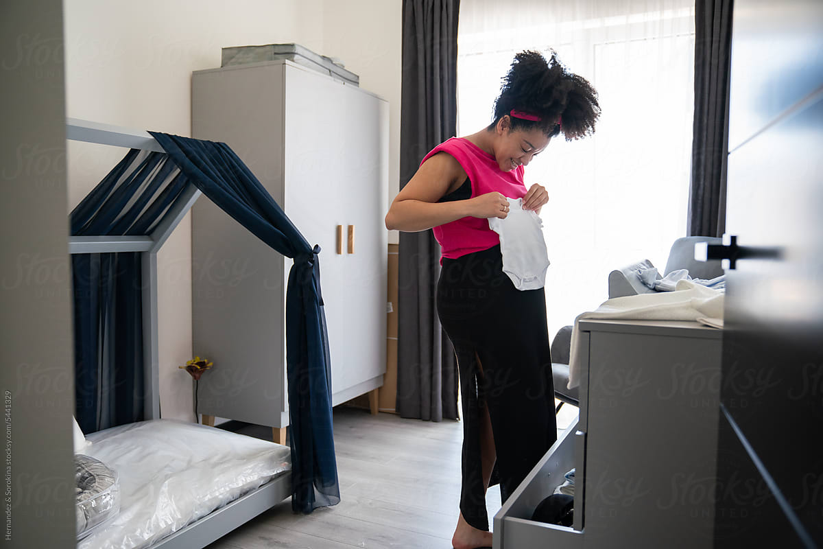 Pregnant Woman Holding Baby Clothes In The Room