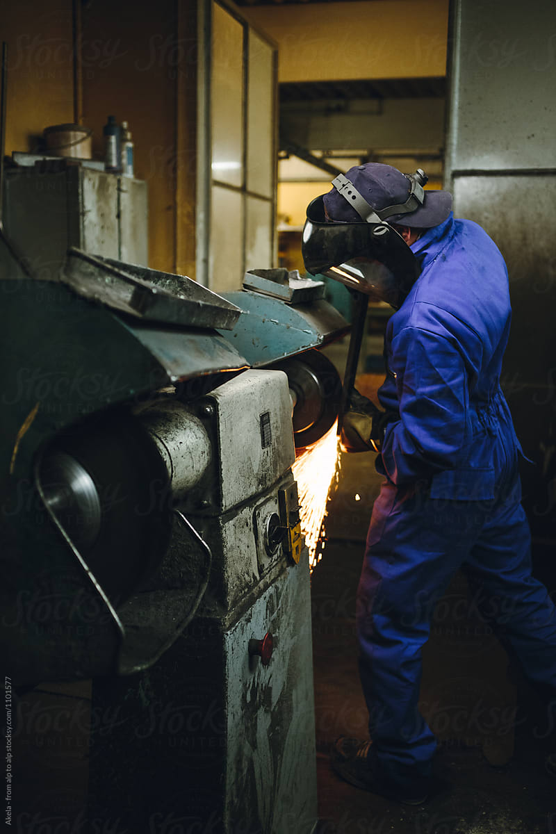 metal worker with protection mask grinding metal plate in a workshop