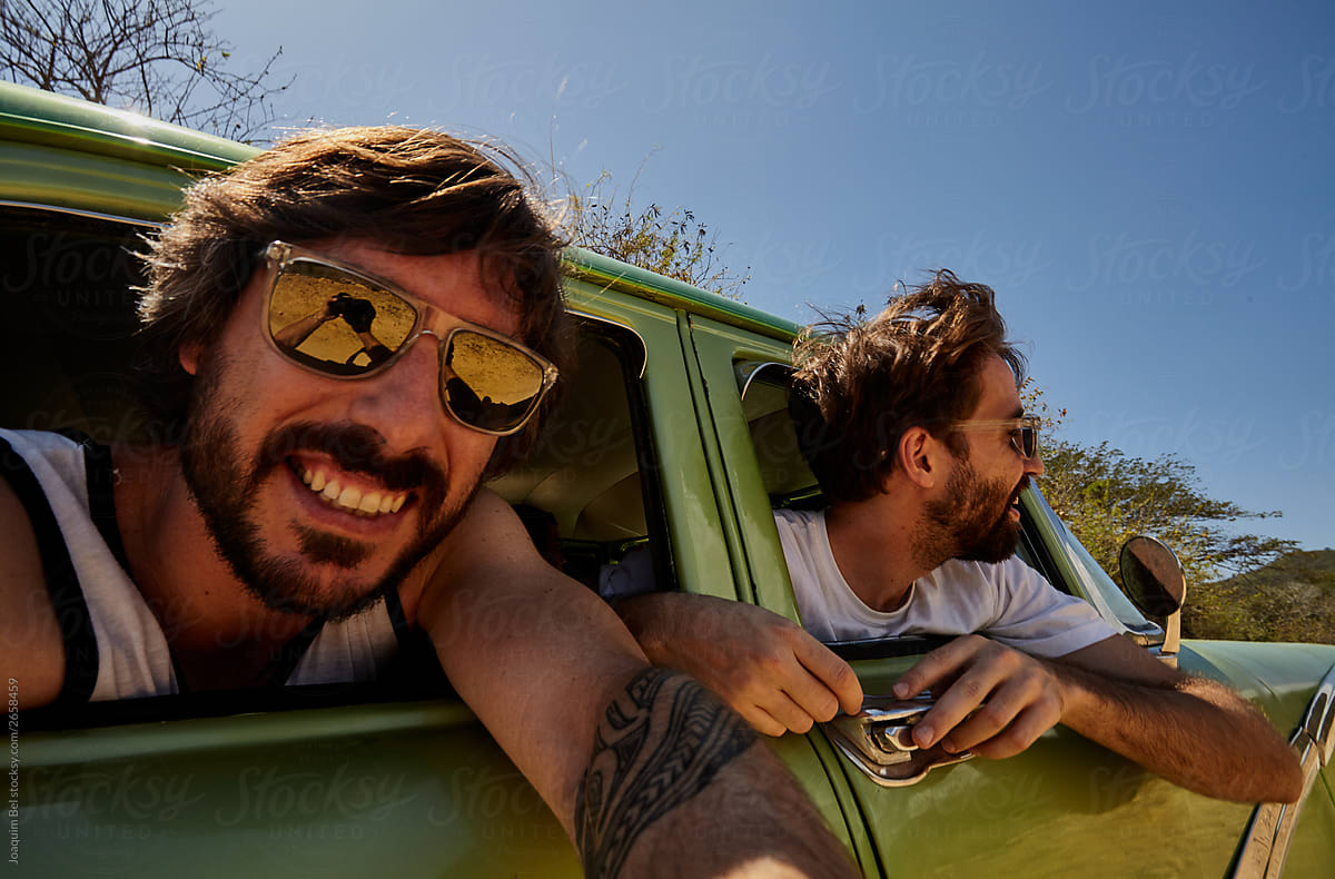 Man in sunglasses taking selfie out of car window with friend