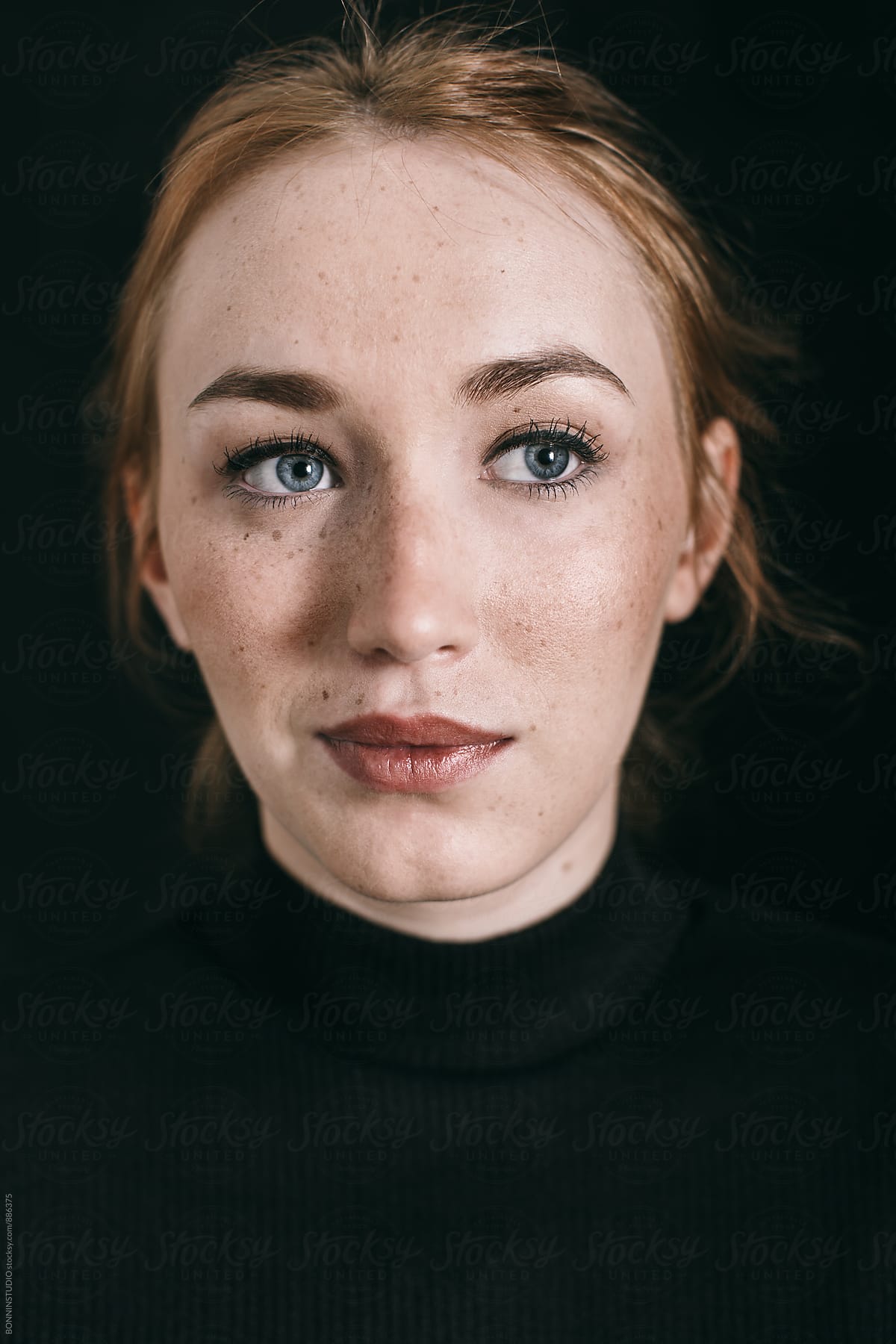 Closeup portrait of a ginger freckled woman on black.