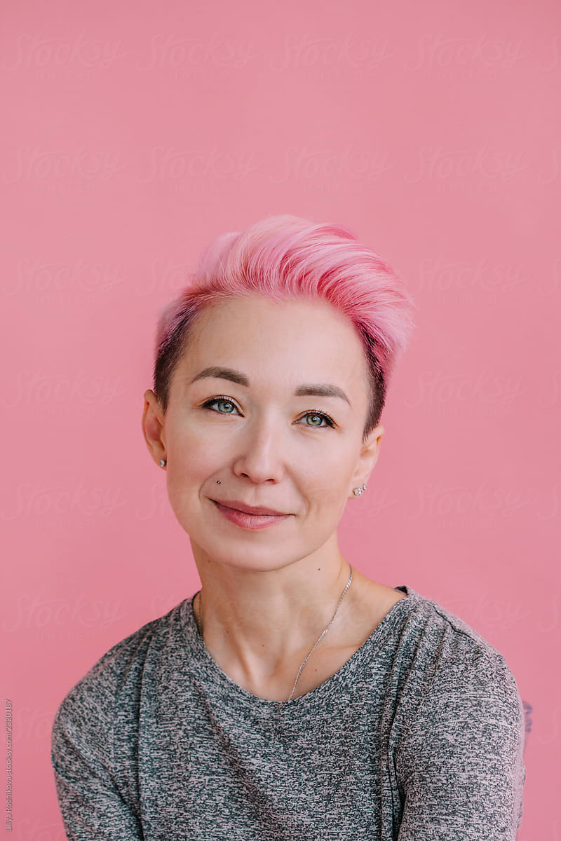 Studio portrait of woman with short pink hair posing by plain pink background