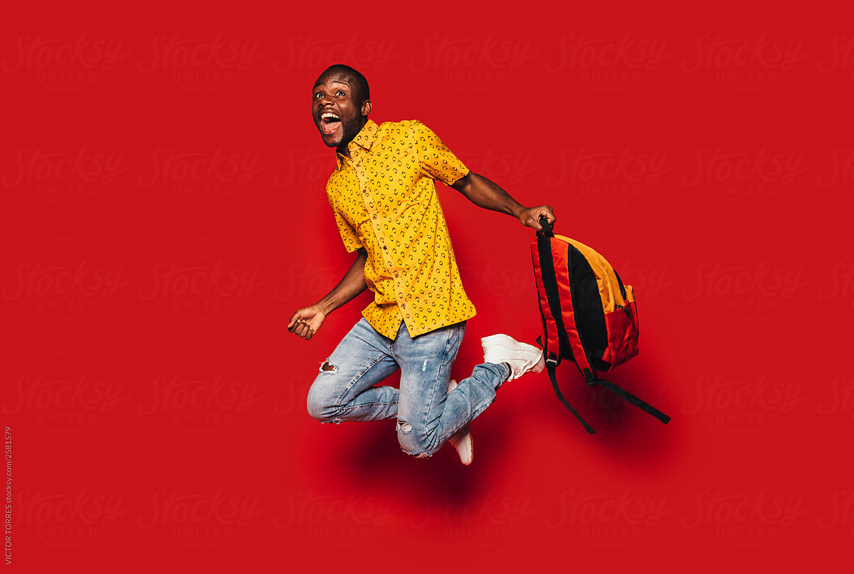 Cheerful young black man jumping with a backpack