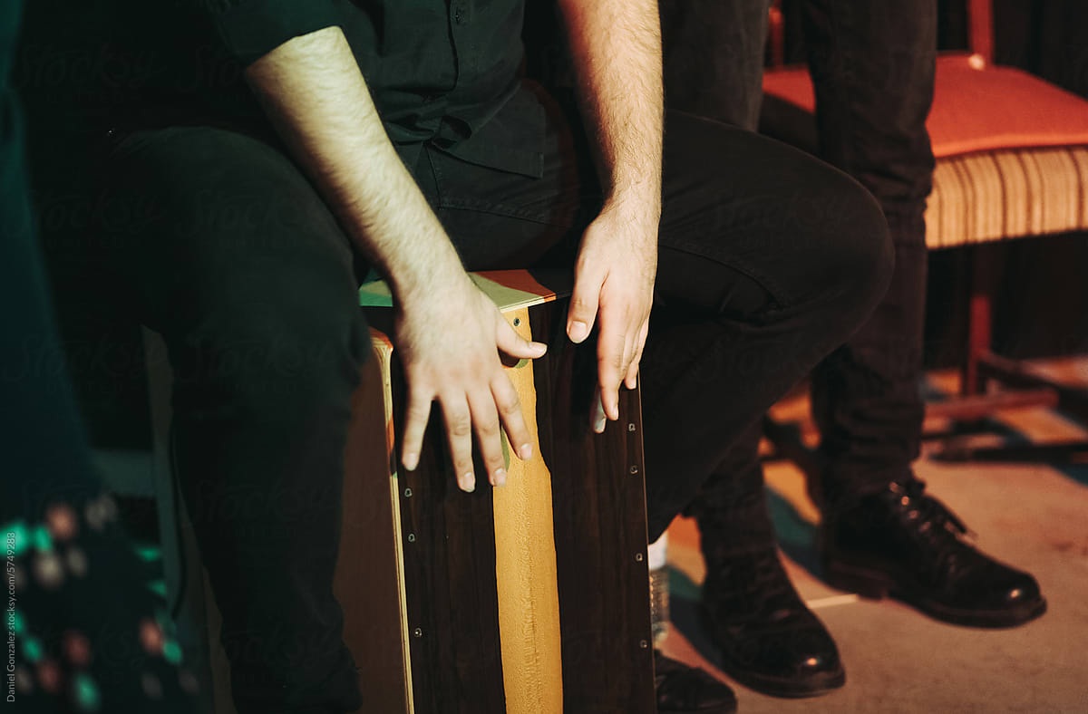 Crop man sitting on cajon box while drumming on stage