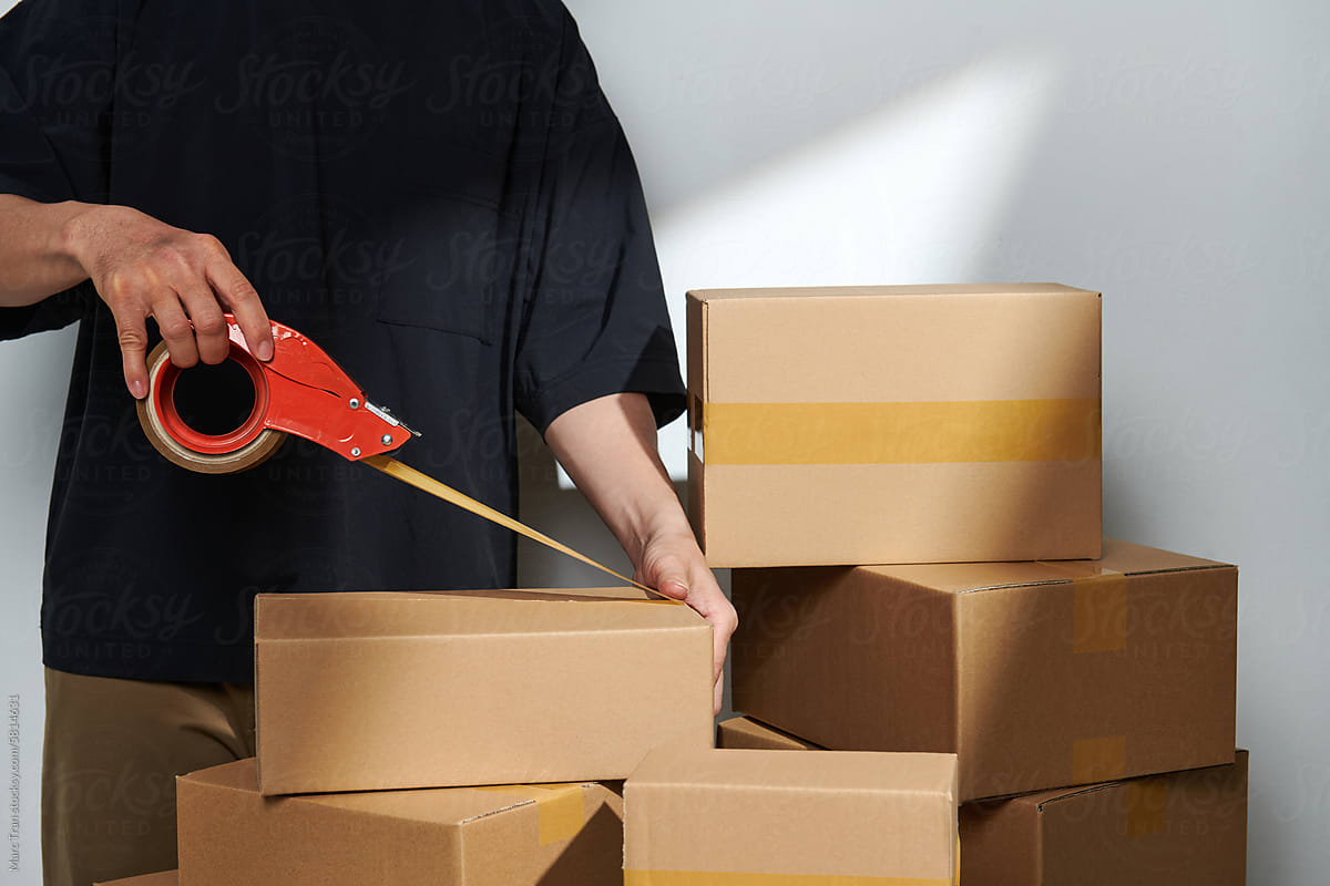 Man sealing a shipping cardboard box with tape dispenser.