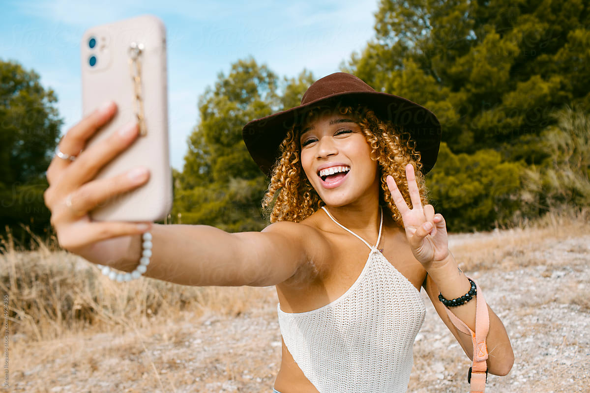 Girl with hat posing for a selfie outdoor in sunlight smiling