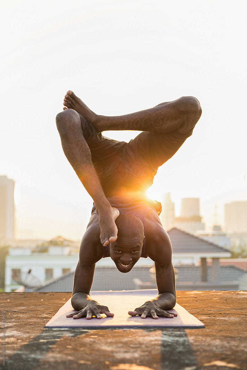 Smiling young man in a scorpion yoga pose outside on a rooftop