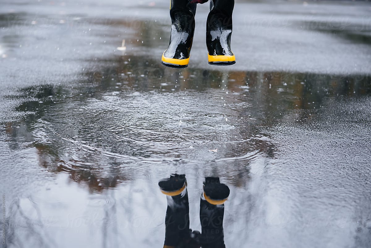Child wearing rubber boots splashes in puddles on a rainy day