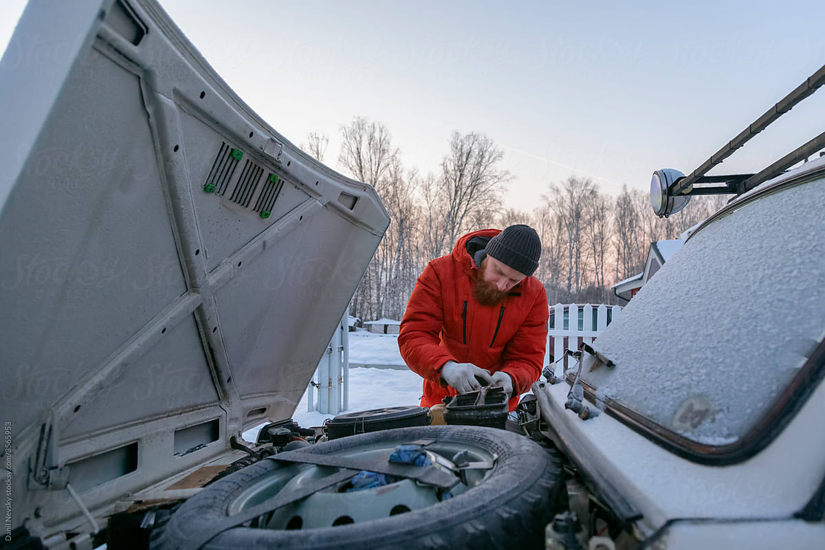 Guy fixing car engine working in snowy rural yard
