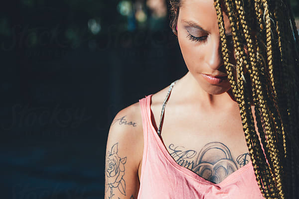 with dark hair cascading down her back in intricate braids and delicate  silver jewelry adorning her ears and neck. Her face is adorned with  intricate tattoos