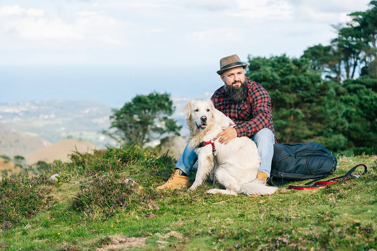 Male traveler sitting on hilltop with dog and backpack