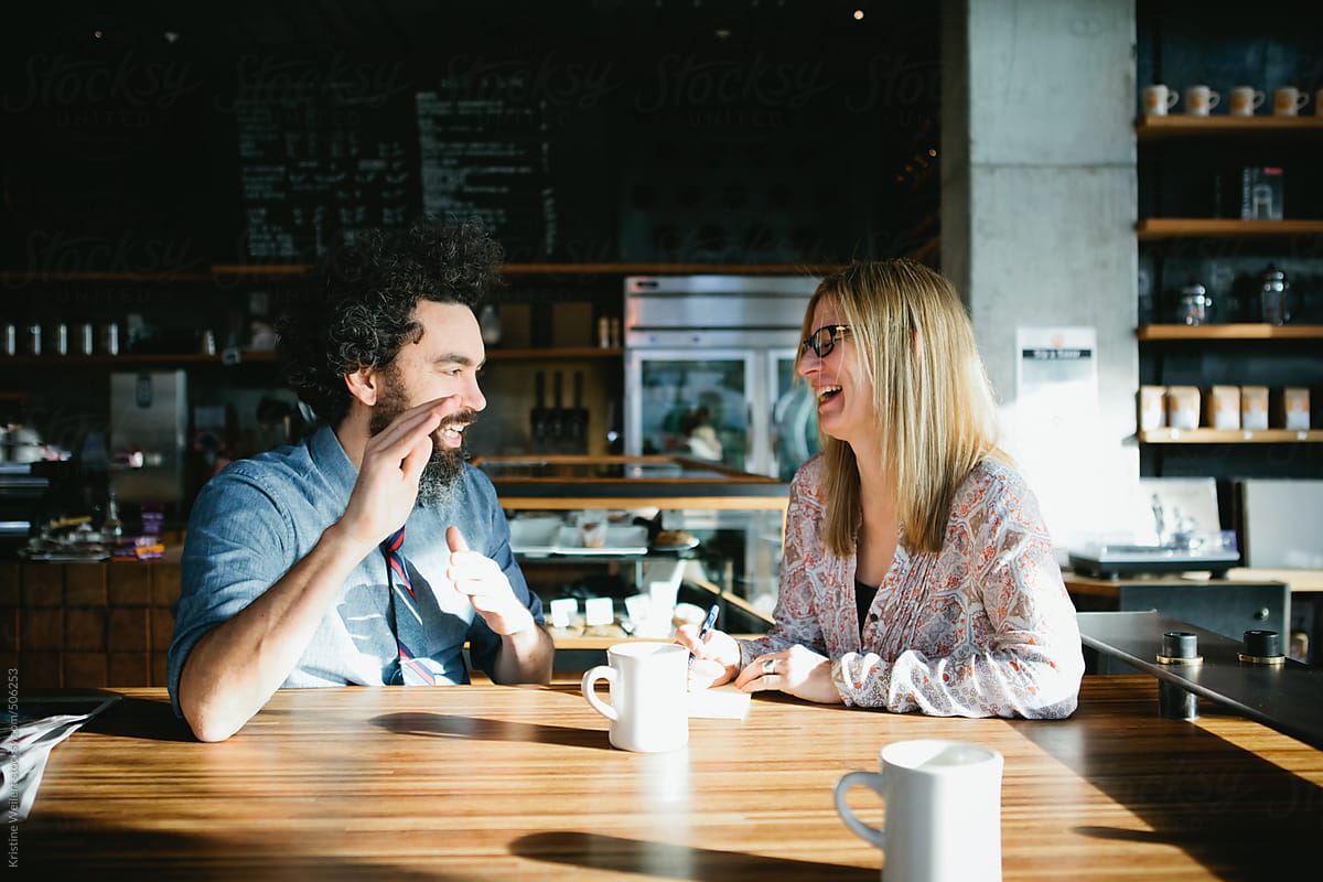 Man and woman laughing while having a conversation over coffee in a cafe