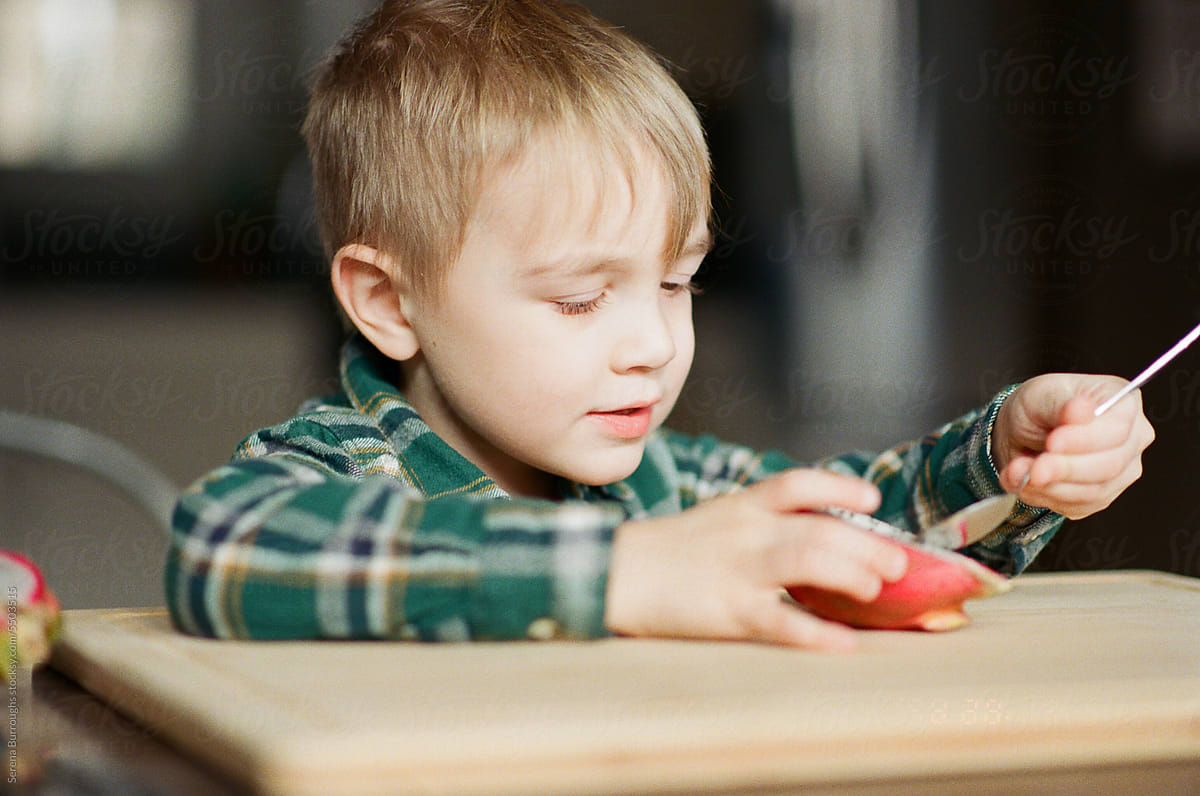 little cute toddler boy eating dragon fruit with spoon independently