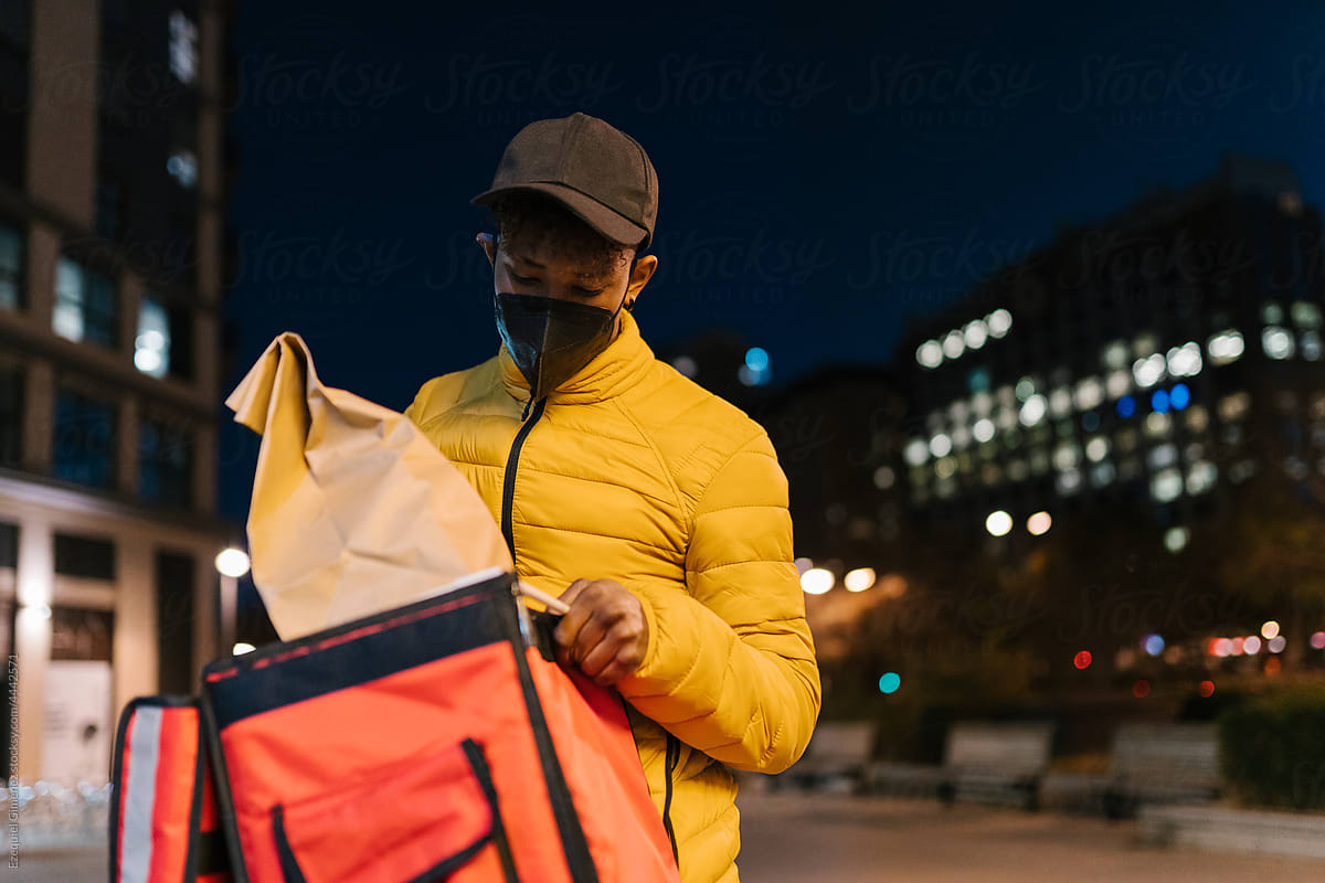 Black courier putting takeaway food in delivery bag
