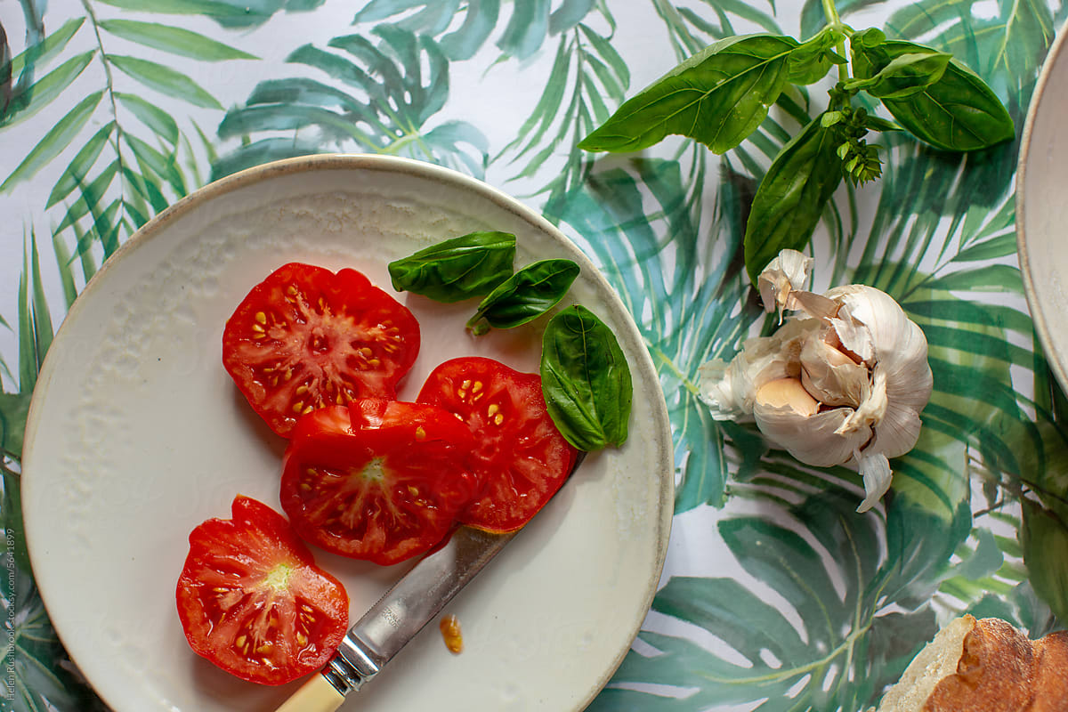 A plate of sliced beefsteak tomatoes with basil and garlic