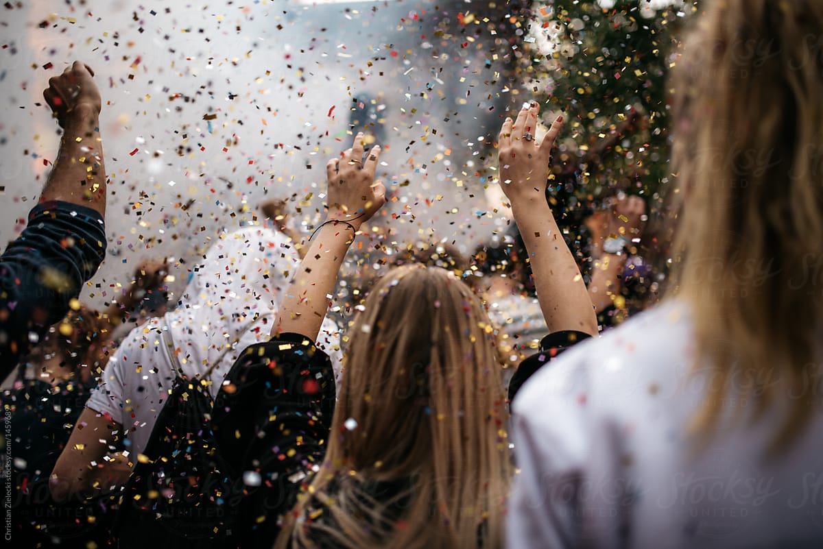 people dancing through confetti at an event raising hands