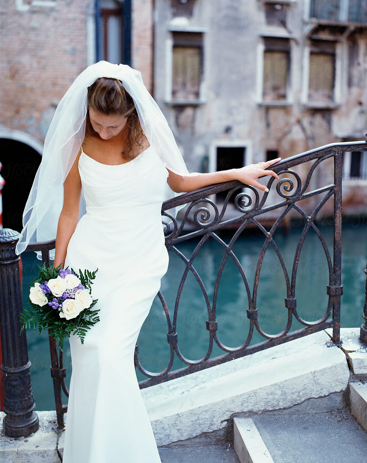 Bride in wedding dress standing next to the canals of Venice.