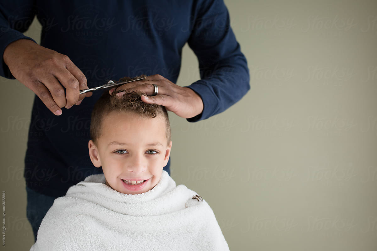 Smiling boy in white towel gets home haircut