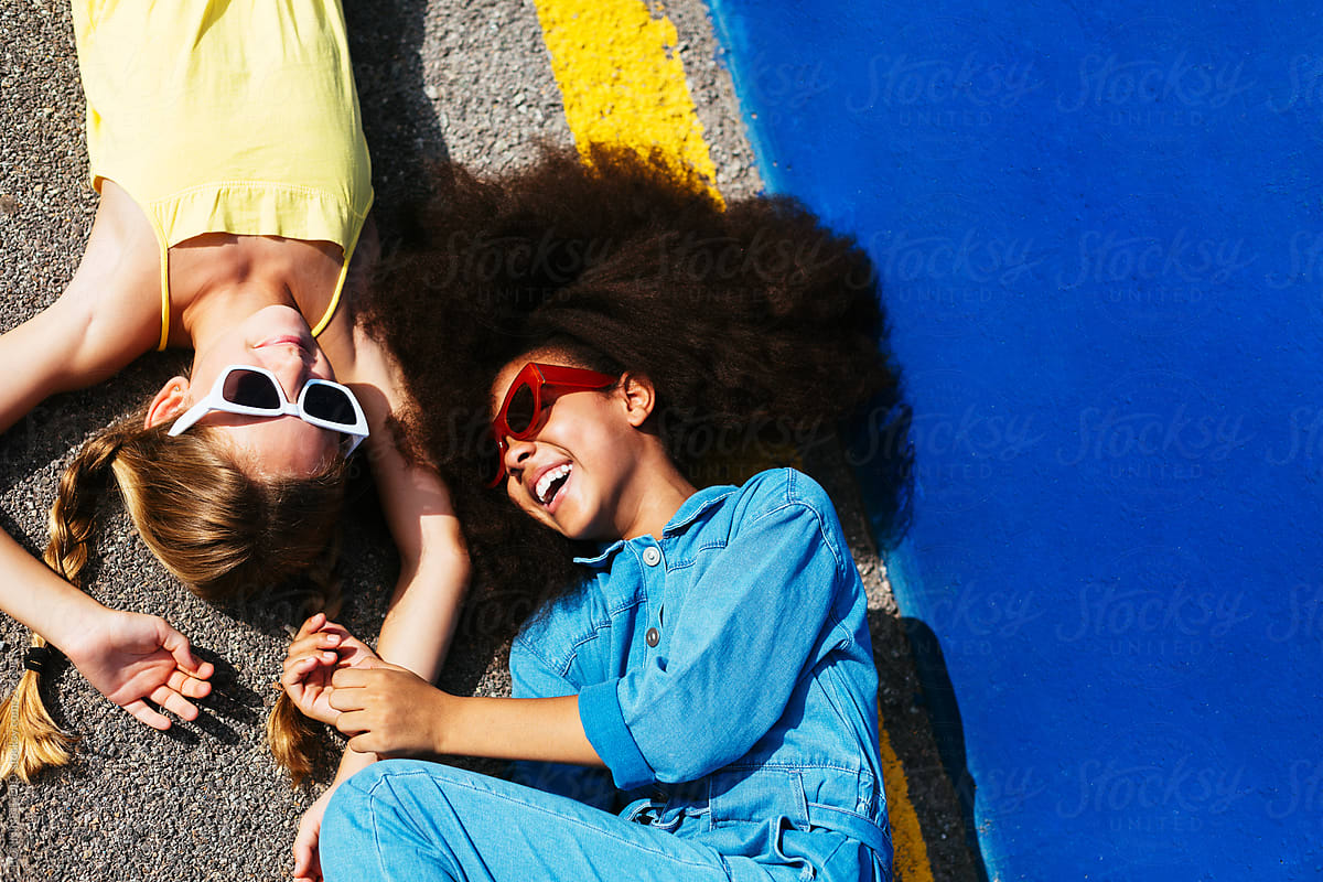 Trendy multiethnic friends in sunglasses having fun and lying on road