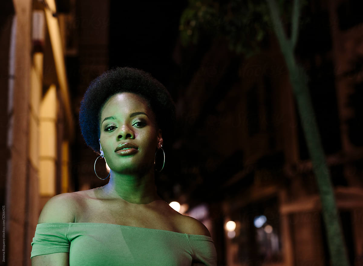 Woman with afro hair standing  outdoors in the city in a summer night looking at camera.
