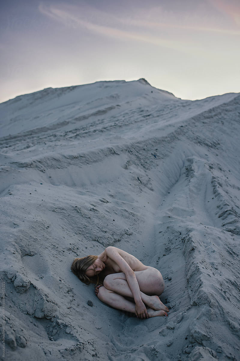 Naked woman lies on the sand in the fetal position
