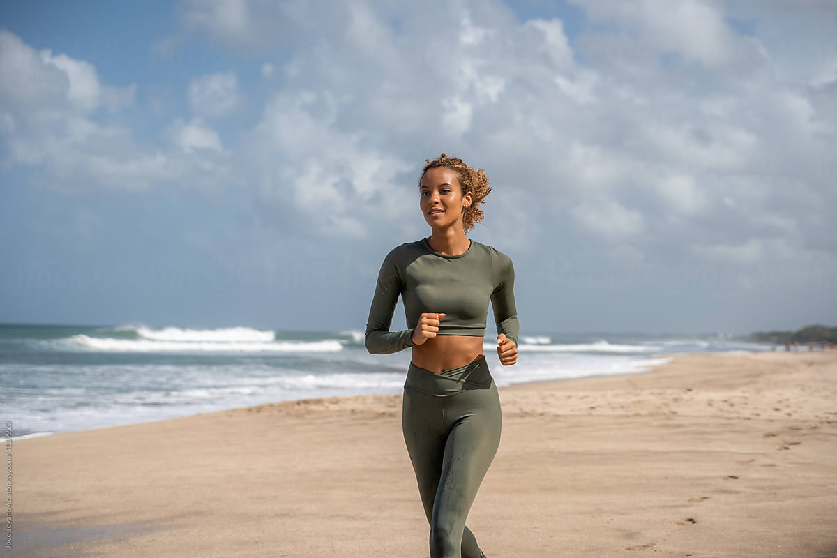 Smiling Self-aware woman in exercise apparel jogging on the sand