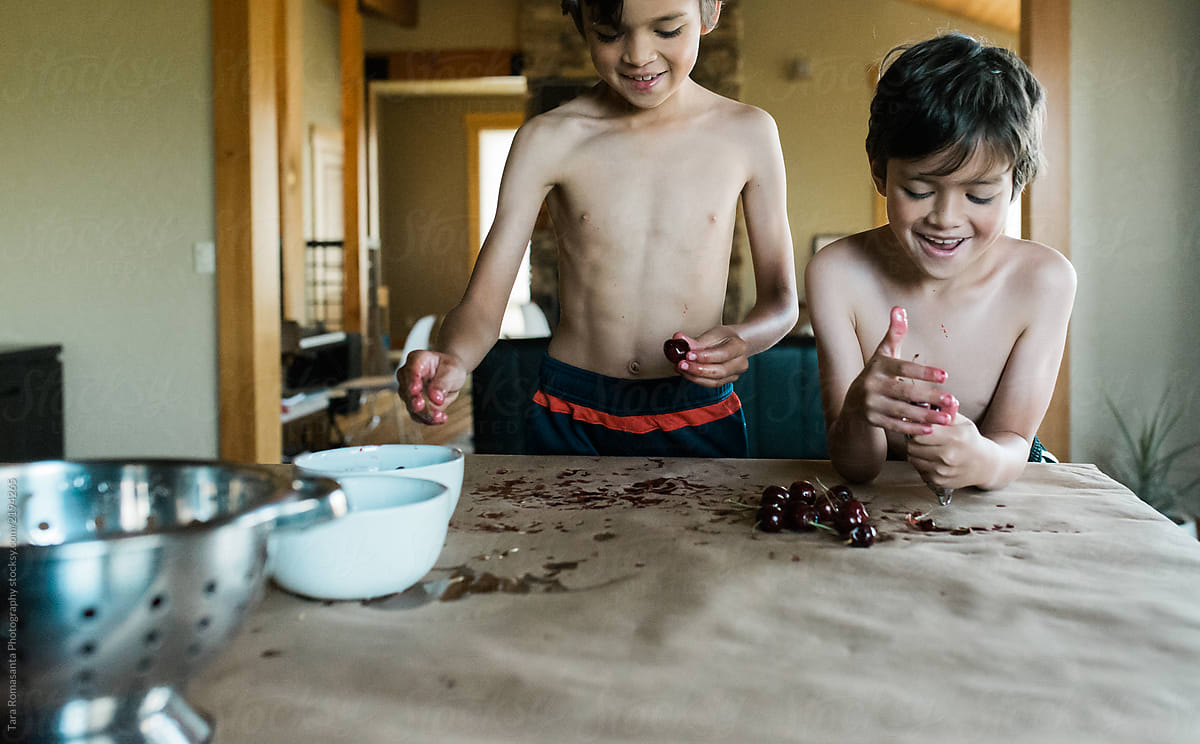 Smiling children helping to pit cherries and make a mess in the kitchen