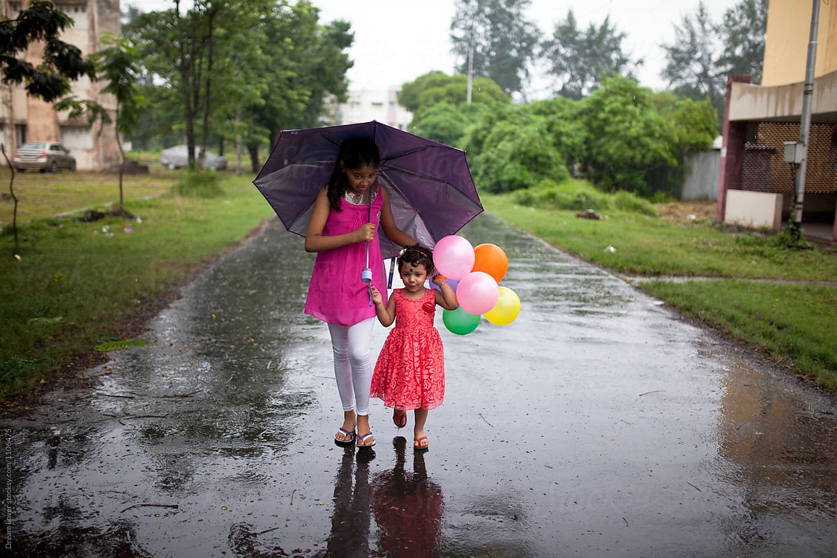 Sisters walking with balloons and umbrella in rainy season
