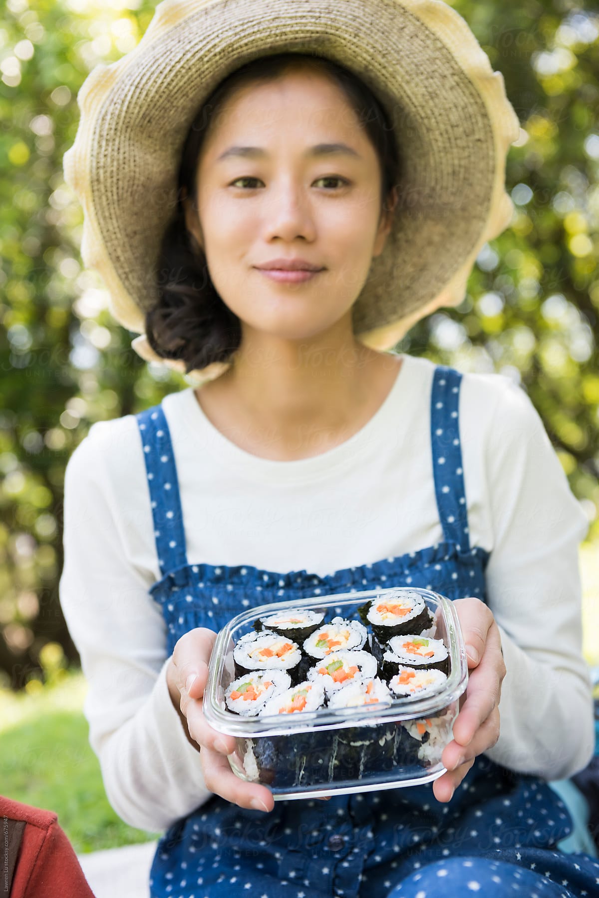 Woman holding sushi in glass container on gree grass in forest