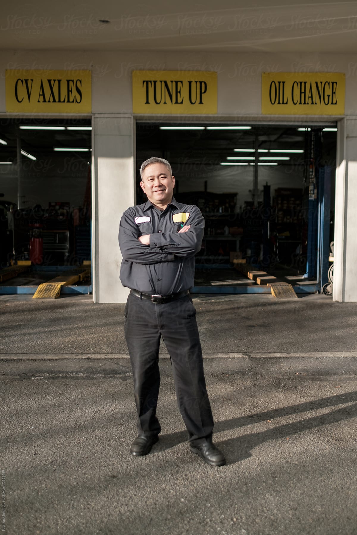 Asian car mechanic standing in front of his auto repair shop