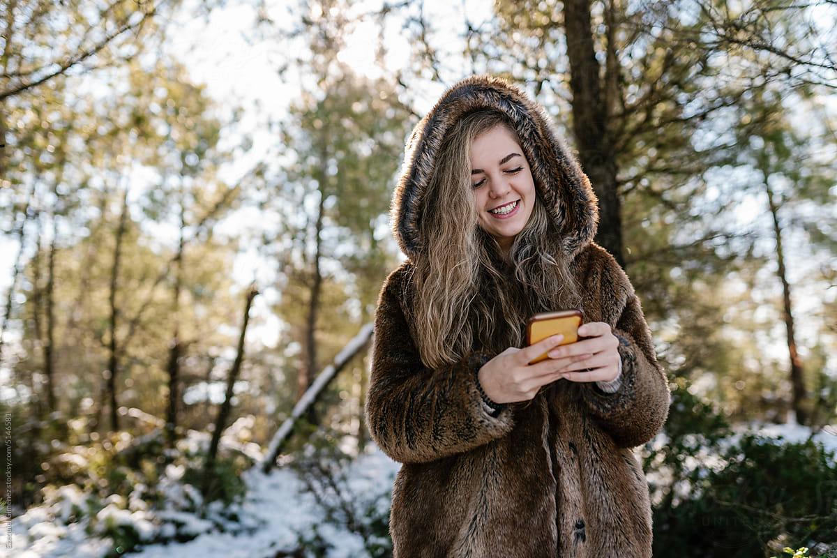 Smiling woman using smartphone in winter forest
