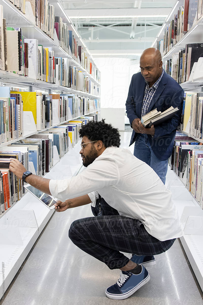 Librarian helping man find book on library bookshelf.