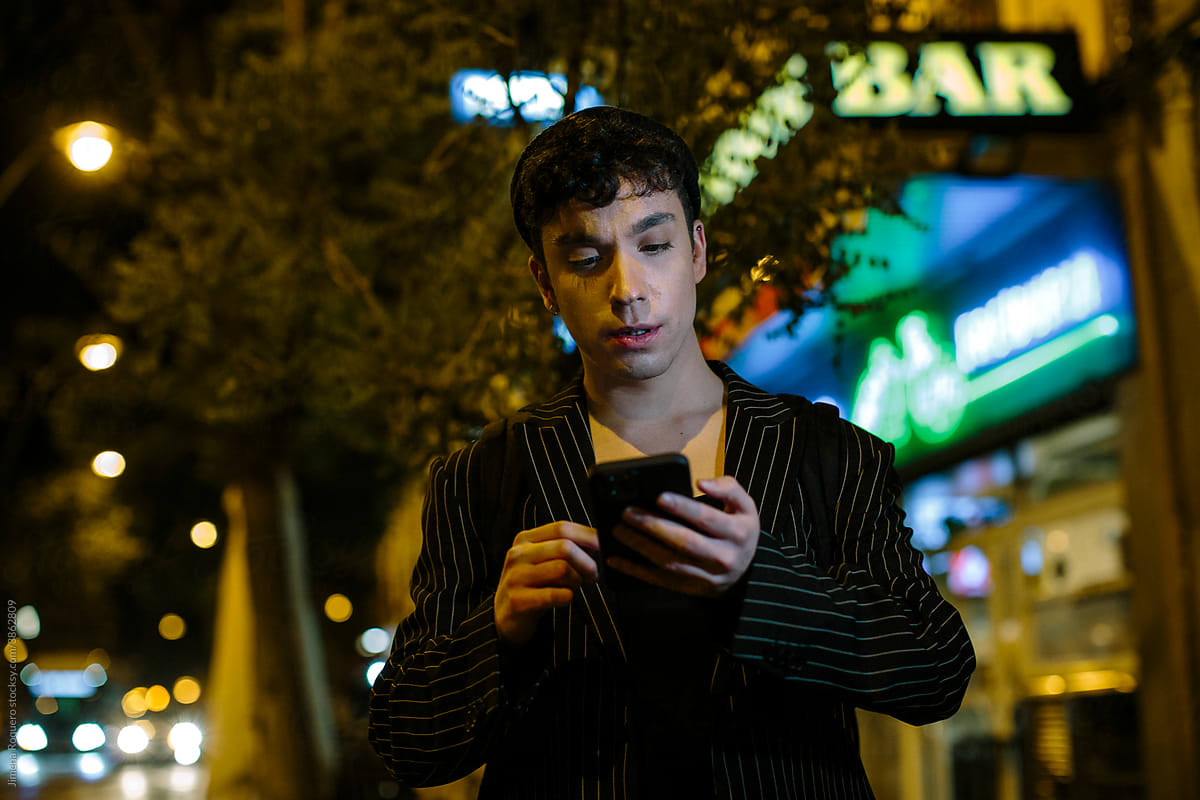 Young non-binary person at night in the city checking smart phone