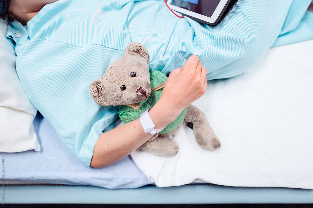 Teddy bear in the arm of a child in a hospital bed