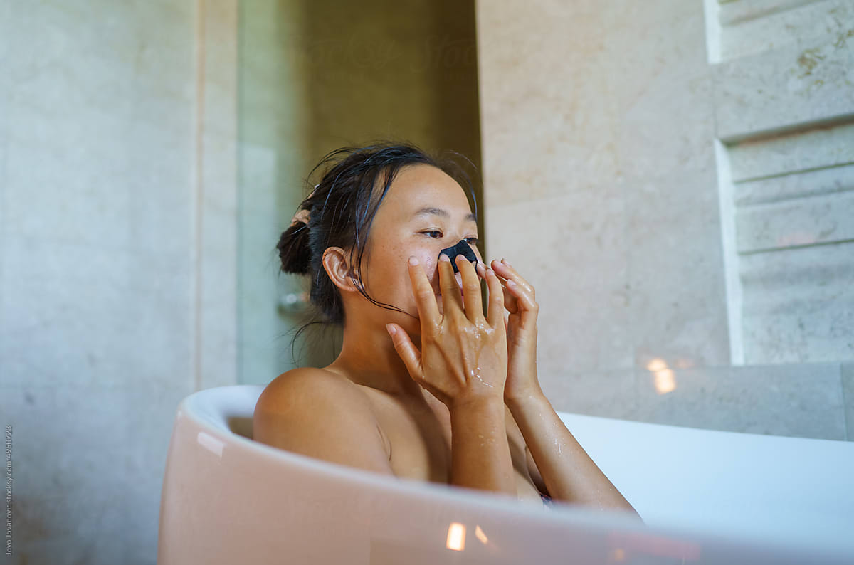 Woman applying nose strip while relaxing in bathtub