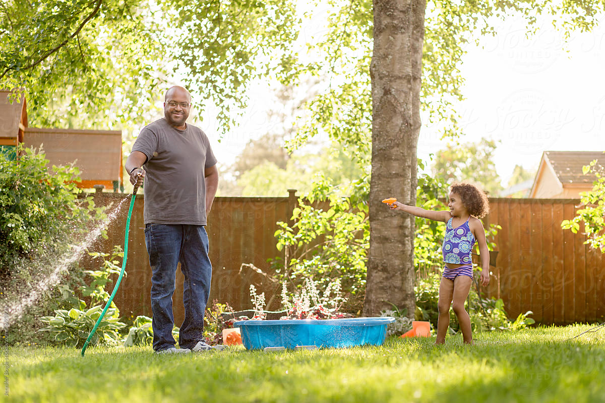 Daughter points water gun at father with hose