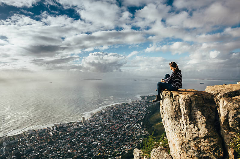 Woman sitting on the edge of a cliff overlooking Cape Town at sunset by ...