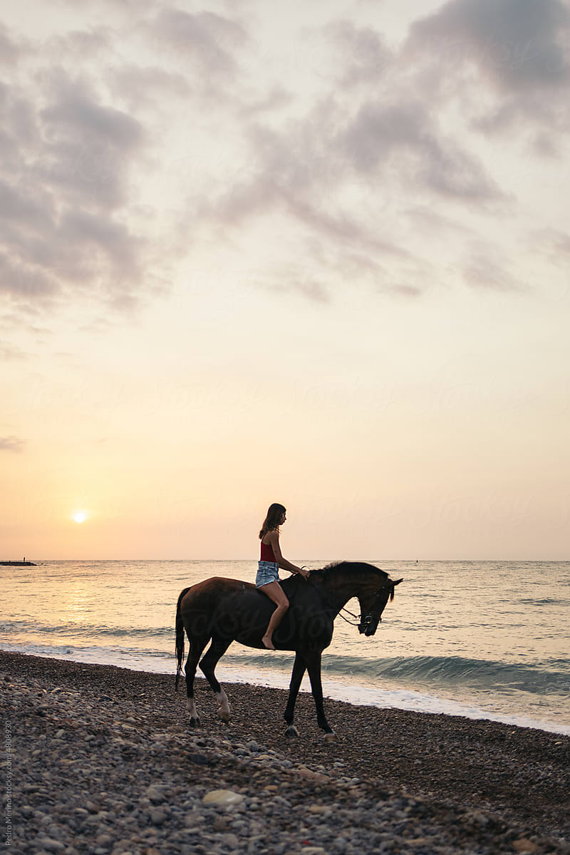 Girl riding a horse on the beach at sunrise