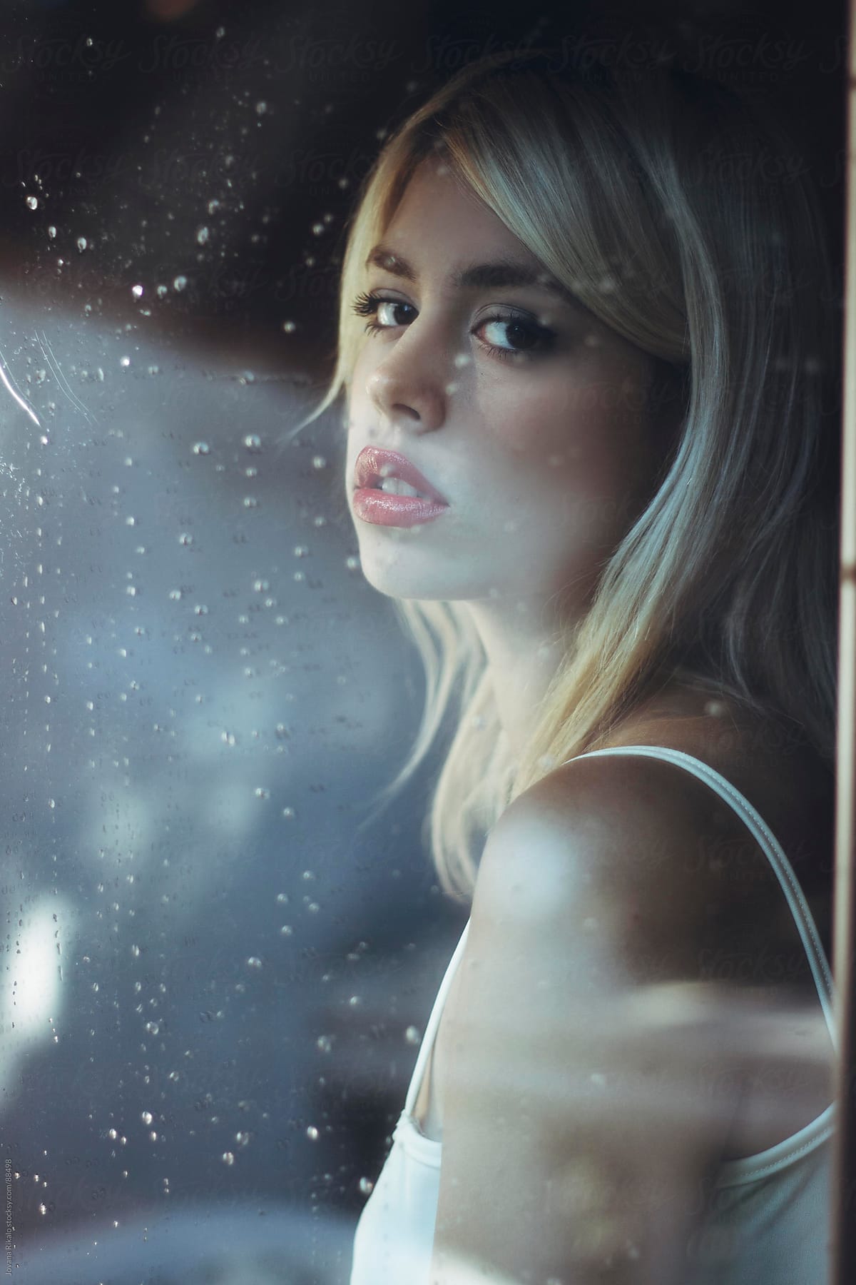 Beautiful girl standing at the window watching the rain