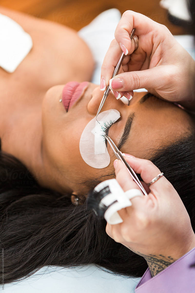 Vertical view of a lash stylist gluing a temporary fake lash to a young black woman