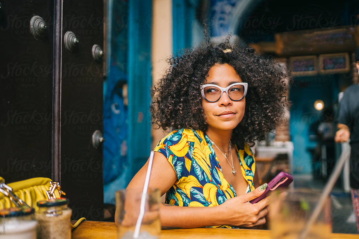 African american girl looking to the side with phone in hands at bar