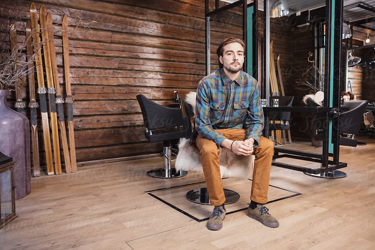 Confident Male Hairdresser With Hands Clasped Sitting On Chair