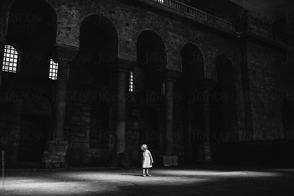 Little girl looks down at her shadow in a large, dark historical building.